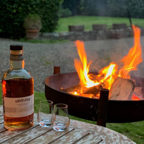 Picture of glasses and bottle of whisky on garden table and firepit